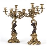1247  A pair of patinated and gilt bronze candelabra
Late 19th / early 20th century, probably French, each surmounted by a single light over a foliate standard issuing six S-scroll arms each supporting a rocaille urn-form light, raised overall on a scroll stem held by a seated putti atop a pierced, scrolling foliate base, 2 pieces, 26.5'' H x 17'' Dia., est: $3000/5000

Provenance: Private Collection, La Jolla, CA.  Condition: Drilled for electricity; wiring deficient. Each candelabrum lacking one arm. General marks, scattered minor oxidation, scratches and rubbed wear commensurate with age. One lacking screw to top of putti's head. Some elements loose; would benefit from tightening.  Your bid indicates acceptance of our Conditions of Sale.  AS-IS.  ALL SALES FINAL