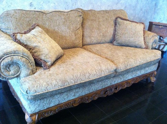 Regal looking couch in shades of golden brown neutral shades with carved wooden accents and armrests. Two throw cushions included.