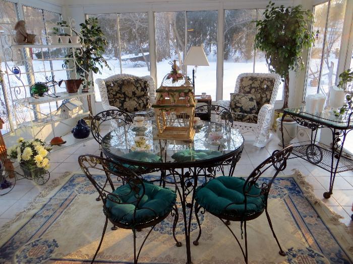 Beautiful sun room full of indoor outdoor furniture.  Included is a bakers rack with glass shelves, iron and glass patio table with chairs and tea cart, wicker chair and rocker.