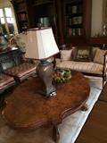             Burled wood cocktail table; 2 matching ottomans/stools pictured to the left of the table; one of many lamps; antique settee