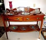Vintage Sideboard with rich finish, serpentine style front, 2 drawer storage with Hepplewhite pulls, and bottom shelf storage; Also shown are some of the collection of Vintage  Rock Crystal Clear Depression Glassware; Vintage Amber Depression Glassware that are available in this sale. This sale has one of the largest collections of Rock Crystal Depression glasswares that we have ever seen.  Items on top of the Sideboard include Vintage Rock Crystal Amber Depression glassware items such as the  Handled Server, and Cake Server, Vintage Hazel Atlas Shot Glass Set, Footed Plateau, Franz Porcelain, Vintage Rock Crystal Depression Footed Dish,  Vintage Accent Table Lamp  / Night Light with cranberry glass globe and lovely hanging crystal lustres ;  Items on the Bottom Shelf include Vintage  McKee Rock Crystal Egg Server,  and Vintage Rock Crystal dishes with gold tone borders.