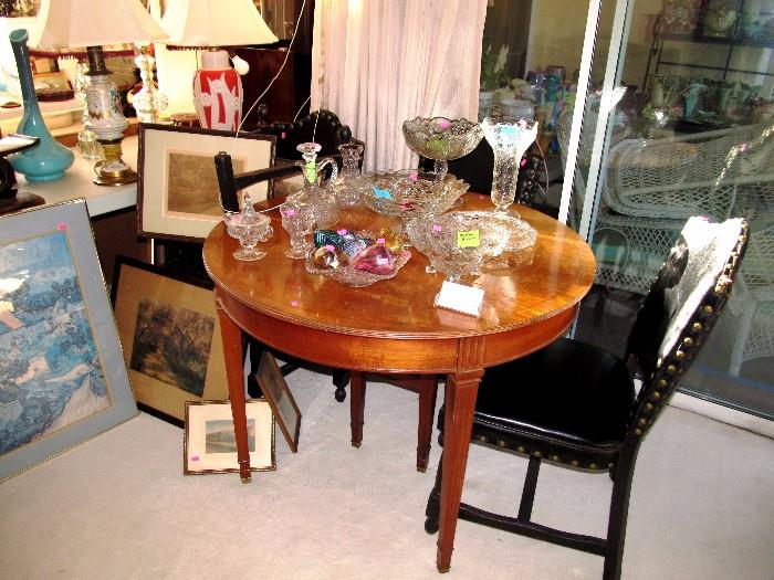  Dining Furniture...Round to Oval Dining Table with light  finish,  3 extra leaves, and brass feet; 4  Dining Chairs with black leather-like upholstery and brass studding;  Also shown are some of the excellent collection of Vintage McKee Puritan Rock Crystal Depression glassware that are available in this sale. Also shown are some of the Vintage Aladdin Lamps  available in this sale.  Also shown are a few of the many good artworks available.