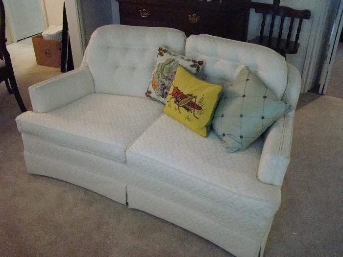 one of two matching white loveseats; needlework pillows