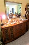 Continental Style Dining Set...includes large dining table with two extra leaves and table pads, 8 matching side chairs with white upholstered seats and woven cane backs with cross hatch style accented tops; matching lighted china cabinet with wood and glass double doors with brass batwing pulls, glass shelves and lower doors storage; matching server. As pictured is the Continental Style Server with 3 drawers and two sets of double doors storage; Also pictured is a large gold tone wall mirror which is also available. Also shown are some of the excellent figurines...vintage Hummels figurines and other Hummel items, porcelain items, and an excellent set of Italian Candleholders with ornate cherubs and florals