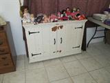 Vintage Shabby Chic Chest with white finish, double door storage, metal hinges and handles, and unique pull up top with storage; Also shown are some of the doll collection that are available in this sale.
