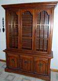 Oak finish china cabinet with glass shelves and interior lighting.