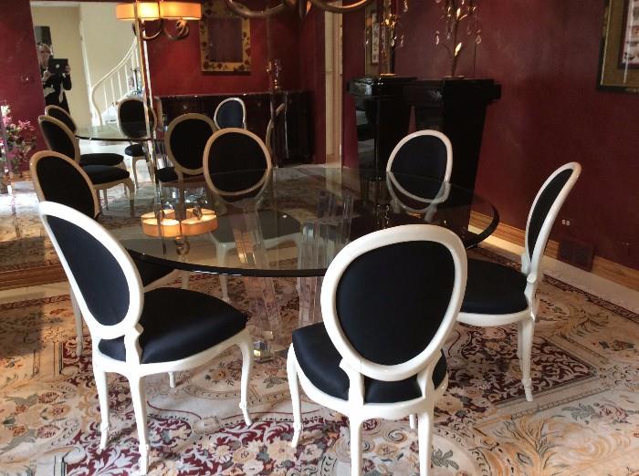Lucite Base Circular Dining Table siz eis  appx 85 inches in diamater glass to is thick with soft beveling edges, The chairs are sold seperately and are done in a gloss white finish with contrasting black upholstery. Area rug is also for sale 9x12 . along with a pari of lucite pedestals.