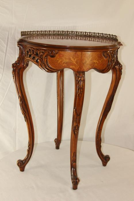 Furnishing – Small side table. Piece is round and wooden with carved trim. Piece has raised metal trim on half the table top. Legs are decorative and curved in. Table top trim is raised on one part. Nice sturdy piece