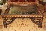 Furnishing – Large rectangular coffee table. Piece has wooden sides and legs. Table top is clear glass. Decorative wooden and metal support under the table top. Piece is in nice condition.