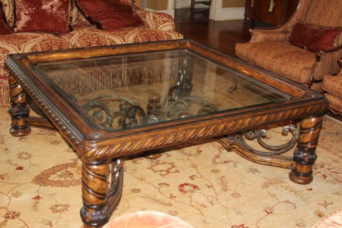 Furnishing – Large rectangular coffee table. Piece has wooden sides and legs. Table top is clear glass. Decorative wooden and metal support under the table top. Piece is in nice condition.