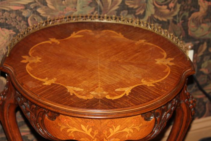 Furniture – Round side table. Piece has decorative legs and lip. Table top is round with different wood coloring making for a lovely piece. Metal trim around half the round table top.