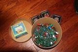 Miscellaneous – Christmas accessories. Round container of Christmas lights, one earthenware snow house cookie jar, and three ceramic candle snow houses. All houses are still in original packaging.