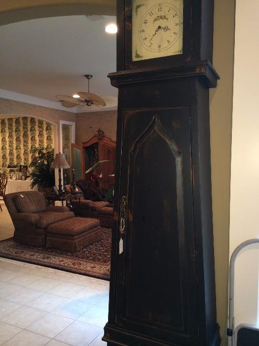 Extra tall decorative clock (not old); in background - two great club chairs with ottomans