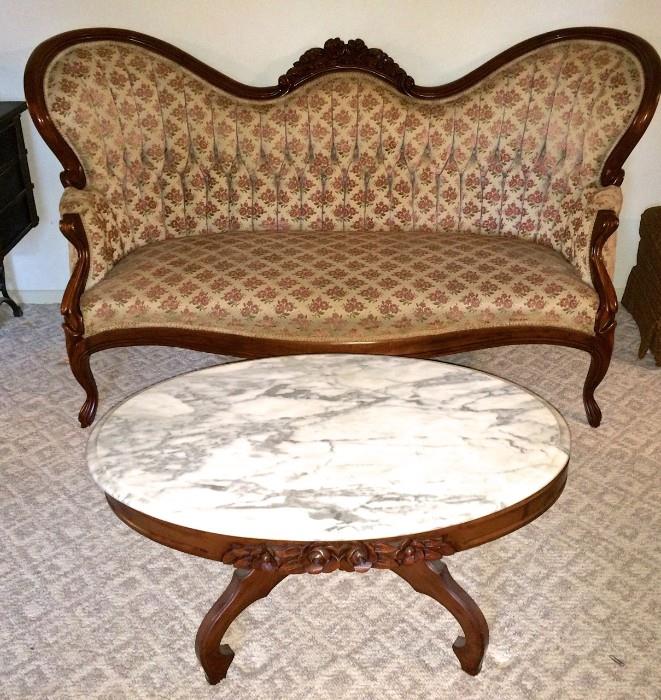 Gorgeous Victorian-style couch with carved-wood detail; upholstery is clean and features bunches of tiny pink raised roses; marble-top oval coffee table with carved-wood detail flanks it