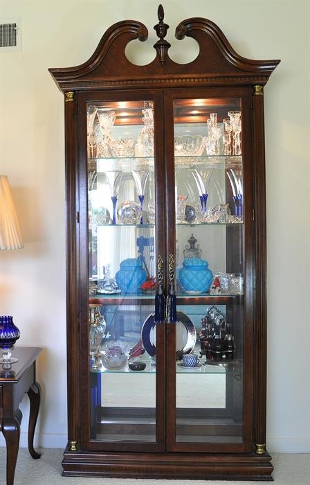 Double door, lighted display cabinet by Pulaski filled  with fine glass by Waterford, Lalique, Baccarat, Sabino, Consolidated Glass and a collection of Waterford Christmas ornaments.