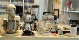 View of some of the appliances - this group has a vintage Art Deco percolator, vintage Sunbeam chrome mixer with juicer attachment and a Kitchenaid professional mixer with juicer and food grinder attachment