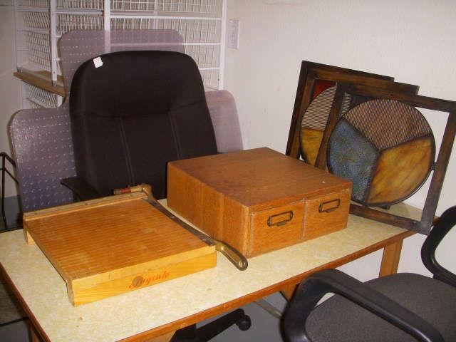 Work table, paper cutter, 2-drawer oak file (no label), wall plaques, desk chairs, etc.