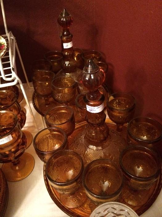 Two amber glass decanters, glasses, & tray sets