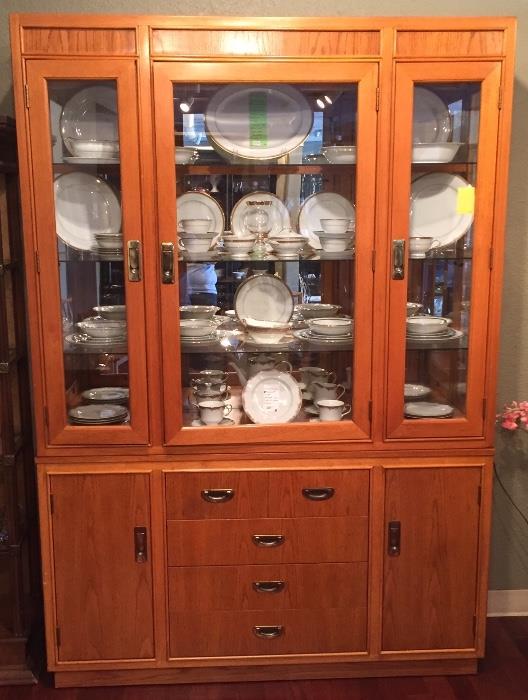 Vintage oak lighted China cabinet with glass shelves filled with Noritake China. 