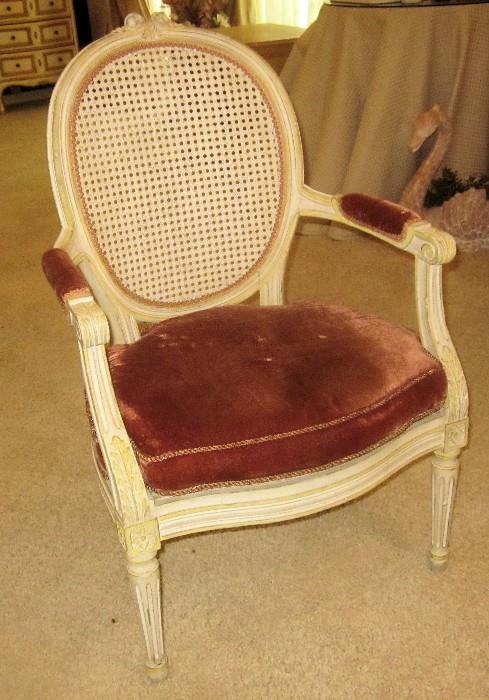 French, cane back and seat, open arm chair with upholstered arms, matching cushion, and curved front. Heavily carved.