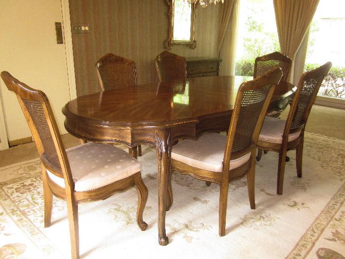 French dining table and six cane back side chairs. Manufacturer is unknown. Table is oval, and has two 20" leaves. With no leaves, the table is 68". With both leaves in place, the table would extend to 108".