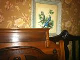 Three antique beds stacked up in front of antique framed print in decorative ornate frame.