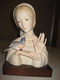 28.	CYBIS Madonna with Blue Bird, circa 1957.     Appraisal Est. $900
Soft cast paste porcelain bust of the Madonna with a Bluebird resting on her right wrist. This is the original Cybis figurine, ( design #20206) produced in 1956-57 and was retired in 1989, and is one of the Biblical Collection Series. She is silently saying, “I Love You”, and for those that read sign language, she is actually signing that phase to the bird, but also to us. She sits on a mahogany stained wooden base, and stands 10” high.
