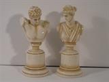 56.	Pair of Porcelain Busts, circa 1950        Pre-sale est. $250
This pair of porcelain busts are of Cicero and Althena. Marked RW in a diamond with a crown. Greek busts on round pedestals. Cicero is6” tall, and Althena is 6-1/2’ tall.
