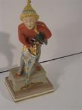 35.	Royal Copenhagen Jester with Umbrella, circa 1945.     Appraisal Est. $400
Porcelain figure of boy, possibly Court Jester, produced by Royal Copenhagen in 1945, determined from the mark on the bottom, Denmark, signed Dgx, and black crown, #1124, titled Mr. Sandman, for Hans Christian Anderson. Boy is matte finish, standing on a pedestal with multi-colored umbrella, with painted designs of swan and woman rising from the sea, tree, and a man. Measures 7” tall, 2-3/4” wide.
