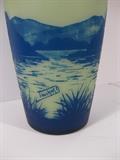 18.	French “Touchard” Glass Vase, circa 1915.     Appraisal Est. $1550
Cameo blown glass, and carved vase, with tapered body and narrowed neck. Chinese styled lake landscape in blue over a white background. Only the neck is carved, while the body has the enamel overlay. Signed “Touchard” on the side of the vase. 12” high.

