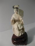 52.	Chinese Carved Ivory Lady, circa 1940.                     Pre-sale Est. $425
Carved ivory figurine of young lady, seated and holding an octagonal fan. Pearls of wisdom around her neck, on a stand of pierced teak. 5-1/2” tall, x 2-1/4” wide.
