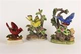 Item Description: A lovely collection of ceramic bird figurines, including one of a yellow bird perched atop a flowering tree branch and another of a blue bird, wings out, ready to take flight, both stamped "Royal Crown". There is also a smaller red bird figurine sitting on a branch, it has a sticker on the bottom that reads "Inarco Japan".

