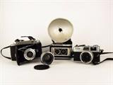 Item Description: A collection of vintage cameras and more, there is a Kodak Tourist II camera with neck strap, a Canon, Canonet 28 with 40mm lens and neck strap, a Kodak Duaflex II with flash holder and plastic strap and a Yashica No. 513840 1:1.8 f=5.5cm auto camera lens made in Japan.
