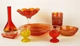 Item Description: An appealing collection of carnival glass and depression ware, includes a footed, scalloped edged candy dish, one red and one yellow glass egg cups shaped like chickens, a marigold colored small bowl with a floral pattern, a pinkish colored little heart dish a red and yellow glass beaker looking vase and more
