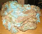 Turquoise Stone Art Sculpture 28" x 24" x 11.5" Beautiful authentic Turquoise stone art sculpture with elaborate carvings. Total weight of the Turquoise alone is 142 Pounds. Signed "A Western View" by Boy Apache and A. Rosell. The carvings are of an eagle, an Indian on horseback chasing a buffalo, bears, a train with an engine and three cars one with black coal, a pueblo village with Indian figures at various jobs, an owl, reindeer, a stage coach with driver and two horses, a bridge for the railroad tracks, another Indian with bow and arrow, cowboy on horseback, plus other superb carvings. The carvings are accented with rhinestone or glass gemstones, metal wire for reins, spears, a metal smoke stack on the train, horns on the reindeer, etc. The sculpture rest on a wooden "Lazy-Susan" with an octagonal glass top which is removable. A very rare piece and one of a kind.
