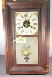 Antique Wall Clock w/ Painted Glass Door
An antique key wind wall clock with glass front door that appears to be hand painted. Clock face has open center and Roman Numeral numbers. Paper label on inside back panel is worn and it is difficult to read the entire name of the clock manufacturer. Weights, pendulum and key are all included. Consignor states that clock is in good working condition. Veneer frame is chipped in several places. Measures 26" tall x 15.25" wide x 4" depth.