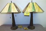 Lot of 2 Classic Mission Tiffany Style Table Lamps
A beautiful lot of two mission style desk or table lamps with gorgeous geometric Tiffany design stained glass shades. Metal base tapers upward to dual bulbs that are controlled separately with their own pull chain. Lamp measures 26" tall and the shade is 20" in diameter.