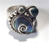 Jewelry Sterling Silver Sajen Colorful Stones Ring
A beautiful sterling silver ladies ring featuring a larger teardrop / pear shaped stone, shell like qualities, multi colored, held in a platform setting by a swirl of sterling silver, with a small teardrop / pear shaped deep green stone, possibly malachite, and a bright light green stone, possibly a green zircon, surrounded by beads of sterling silver varying in size. Marked / signed "Sajen", fits a finger size 8.25.
Total weight: 0.46 ozt
