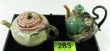 Lot of 2 Vintage Asian Teapots
Lot includes:
- A vintage piece of pottery, marked with an Asian symbol on the bottom. The pink and green color teapot features a handle with was molded and painted to resemble a tree branch. The spout has a flower petal design. Sitting atop the lid of the teapot is a winged insect, possibly a cicada. The teapot measures 5.5" tall with a 3.5" diameter lid. There are several small stress cracks around the top of the teapot but they haven't broken.
- A brown and green teapot / decanter featuring a robed man who seems to be hugging the jug. The front of the vessel has Oriental style writing on it. There are no manufacturing marks on this piece. Measures 6.75" tall.