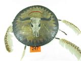 Native American Indian Rawhide Shield
A hand crafted Native American Indian shield made of rawhide and decorated with a steer skull and lightning shaped arrows. Has three hanging feathers and one hanging of animal hair. Measures 17" in diameter. Used condition, feathers are frayed and there is a scratch across the front top. The back is signed with a cow skull symbol inside a diamond.