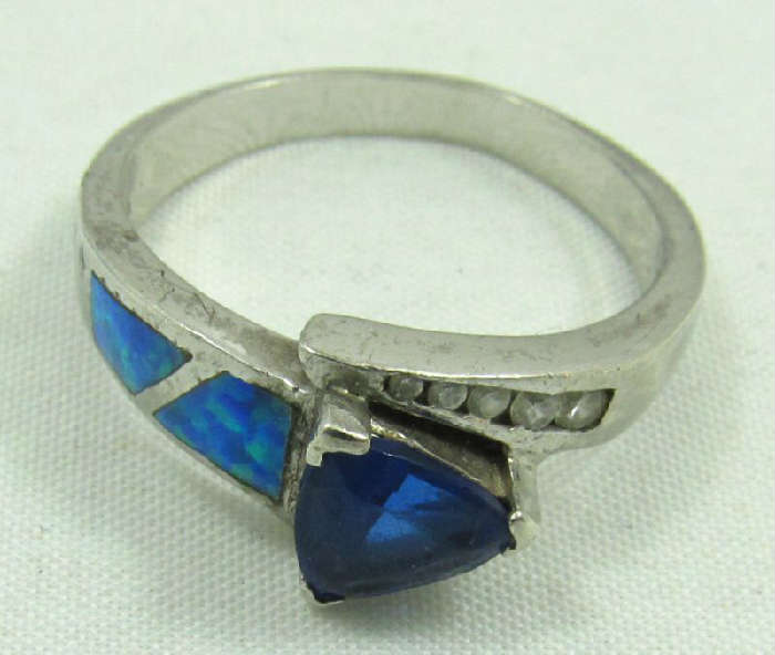 Jewelry Sterling Silver Opal & Sapphire Ring
Gorgeous sterling silver fashion ring featuring inlaid opal stones, clear gemstones and a blue colored stone, possibly a blue sapphire. Main stone shows signs of wear. Marked "925", ring size: 9. Total weight: .14 ozt.