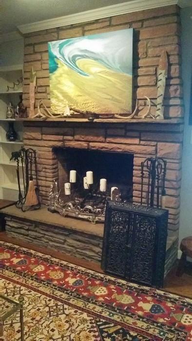 Another Marilyn Suriani original artwork above the stone mantel, deer antlers, wooden fish, two sets of fireplace tools, an antique cast iron door from a wood stove and an antique fire fender...