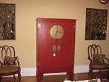 A red armoire with brass fittings flanked by heavy wrought iron covered mirrors and matching arm chairs with animal print seats.