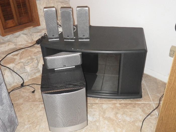 JBL Home Cinema Speaker System (other speaker still attached to wall) sitting on tv stand with glass door