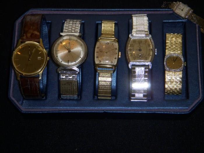Watches.   Four Men's watches are (left to right), 14 karat solid gold Omega Seamaster, Bulova Accutron, Lord Elgin gold filled 21 jewel, 1928 Bulova.  Woman's watch is gold, but has a small band