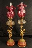144 - Pair French bronze figural cupid lamps with ruby red shades, still oil.
