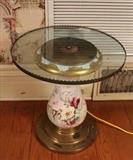 389 - Round glass top table with floral painted base, 23 in. T, 21 in. R.
