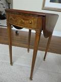 MAITLAND - SMITH PEMBROKE STYLE MAHOGANY AND FRUITWOOD INLAY DROP LEAF TABLE, H 27", W 31", D 19":having ribbon and bell designed inlay; fluted and tapered legs, brass pulls, and casters; 16"W. with leaves in folded position;