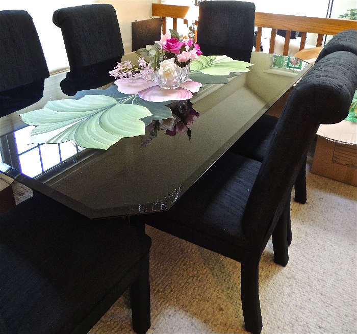 Elegant seven piece contemporary dining set in basic black. Glass top table (shown here with floral table runner), and six rich black side chairs upholstered in a textured slubby fabric.