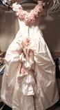 Back view of romantic wedding ball gown by Ron Lovece with deep V-neck framed by pastel roses, princess seamed fitted drop-waist bodice, full skirt with train (shown here bustled). As wedding gowns tend not to run true to other garment sizing, we will say this is a size P-S. The bodice of this vintage c. 1980's gown is very fitted and measures approximately 30". Original price of this gown was $4700. Included with the gown are the crinoline and veil with headpiece.